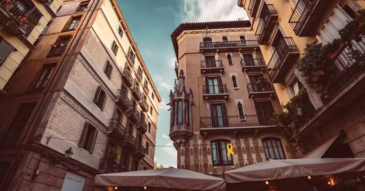 Explore the historic architecture of a vibrant Barcelona street with charming balconies and a blue sky backdrop.