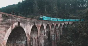 A blue train traverses the iconic Nine Arch Bridge in Ella, surrounded by lush Sri Lankan forests.