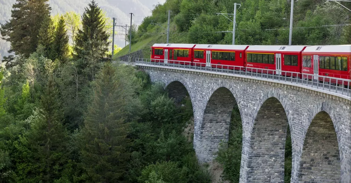 Stunning view of a red train on a viaduct in the lush Swiss Alps, showcasing beautiful nature and engineering.
