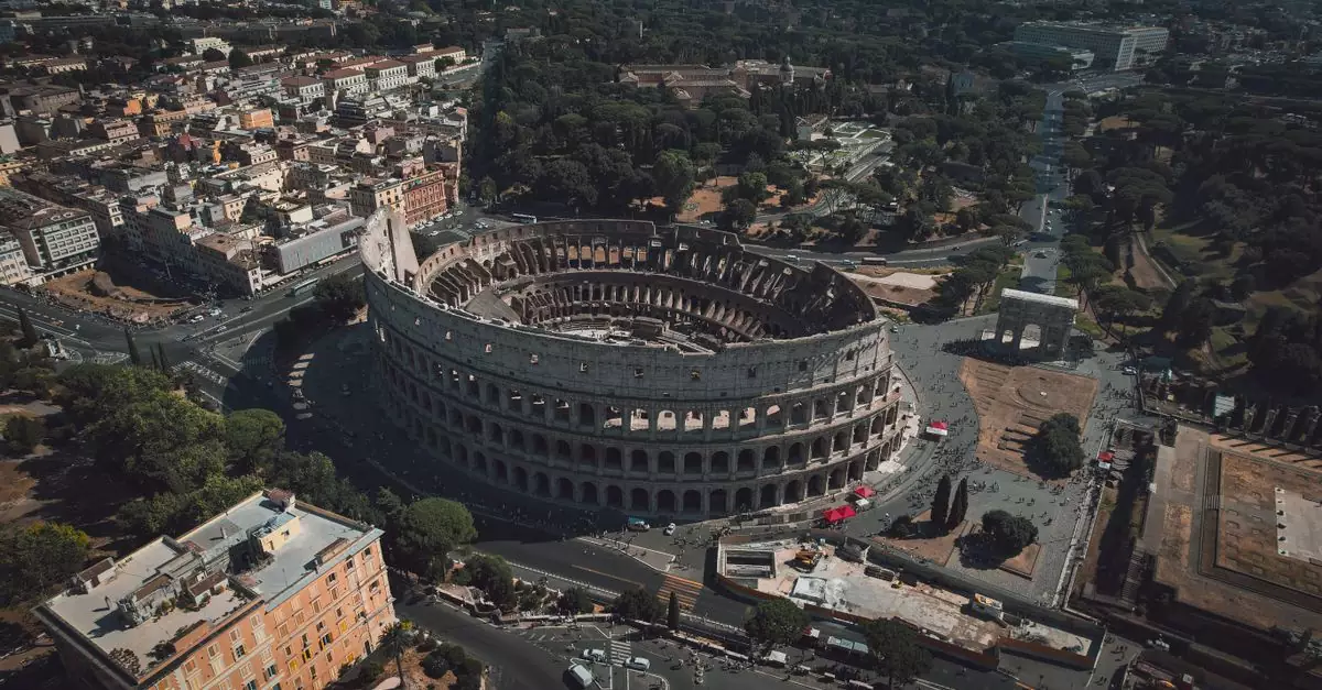 High angle drone shot of the Colosseum in Rome, Italy, showcasing its grandeur and surrounding urban landscape.
