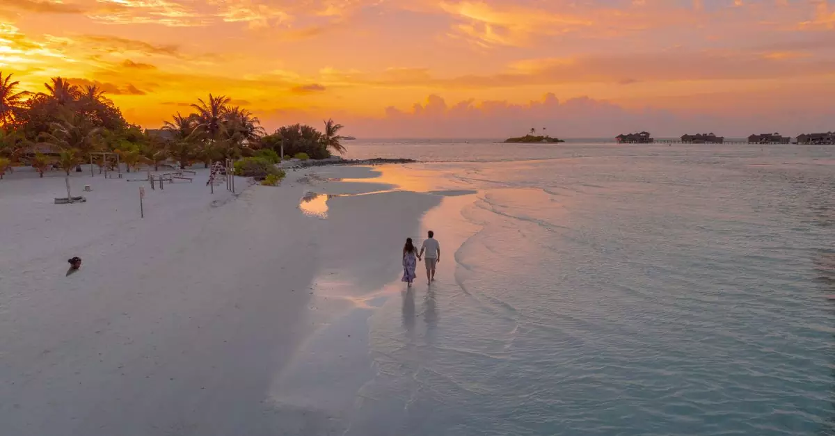 A couple walks on a serene Maldivian beach at sunset, capturing romance and tranquility.