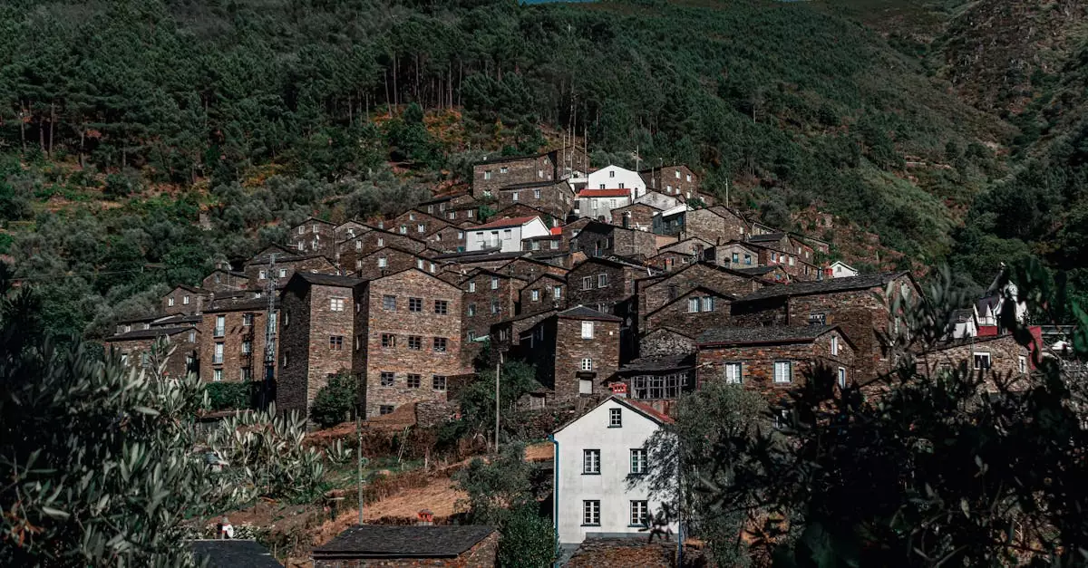 A picturesque village with stone buildings set amid lush, green hills and dense forests, under a clear blue sky.