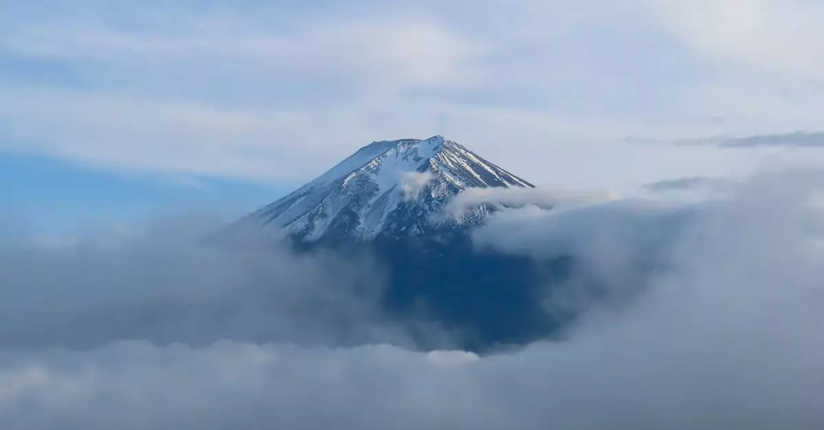Majestic view of Mount Fuji with its snow-capped peak surrounded by clouds under a clear blue sky.