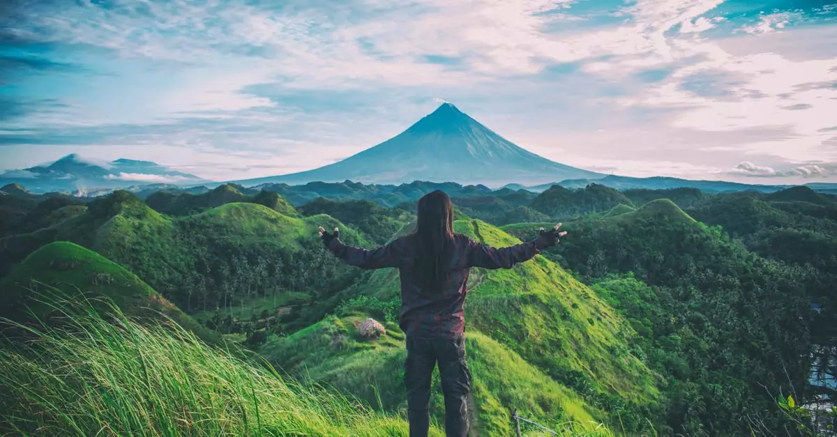 A person enjoys an expansive view of Mt. Mayon amidst lush green hills in Bicol, Philippines.