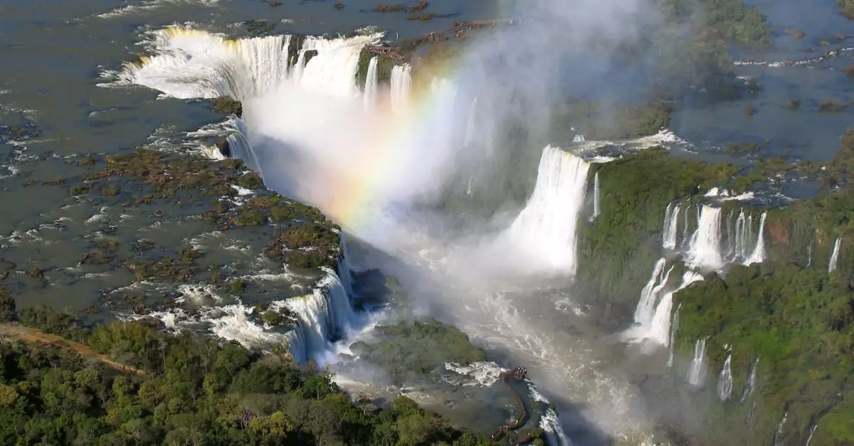 Stunning aerial view of Iguazu Falls cascading with a vibrant rainbow and lush greenery.