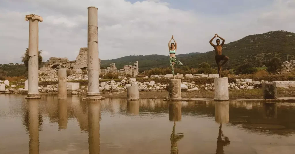 Best Wellness Retreats in South America for Rejuvenation 3 Two people practicing yoga poses on ancient stone ruins beside water. Reflective and serene atmosphere.