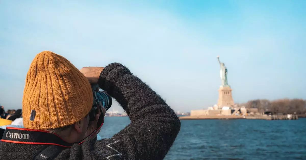 A person in a beanie capturing the Statue of Liberty across the water in New York City.