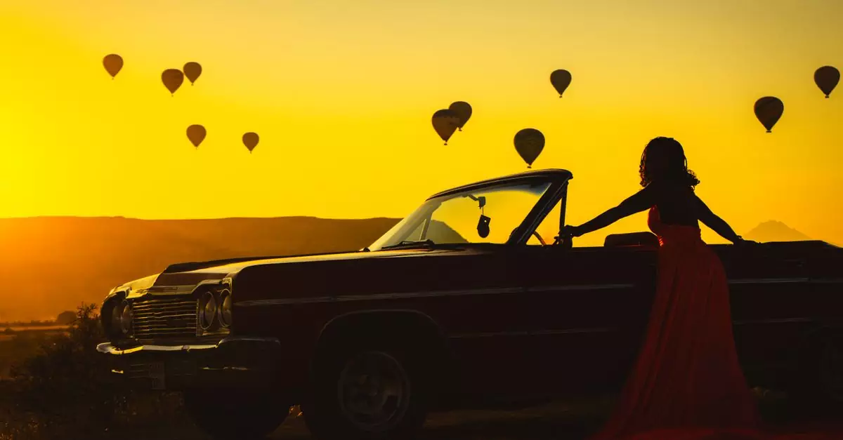 Silhouette of a woman by a classic car with hot air balloons at sunset in Cappadocia, Turkey.