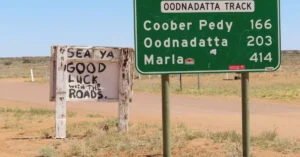 Road signs on the Oodnadatta Track in the Australian outback, featuring humorous local signage.