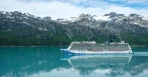 A majestic cruise ship sailing through clear waters with snowy mountains as a backdrop.