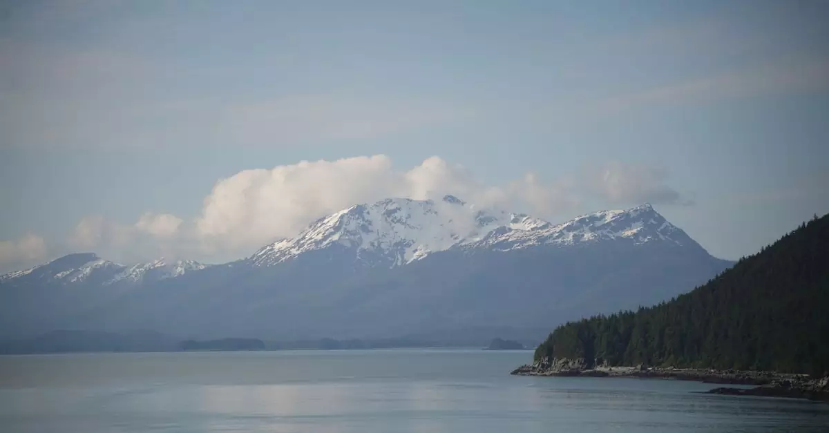 Majestic view of snow-capped Alaskan mountains and tranquil waters under a clear sky.