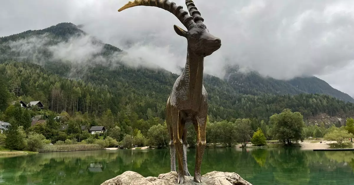 A majestic statue of an ibex on a rock by a serene Alpine lake surrounded by lush mountains.