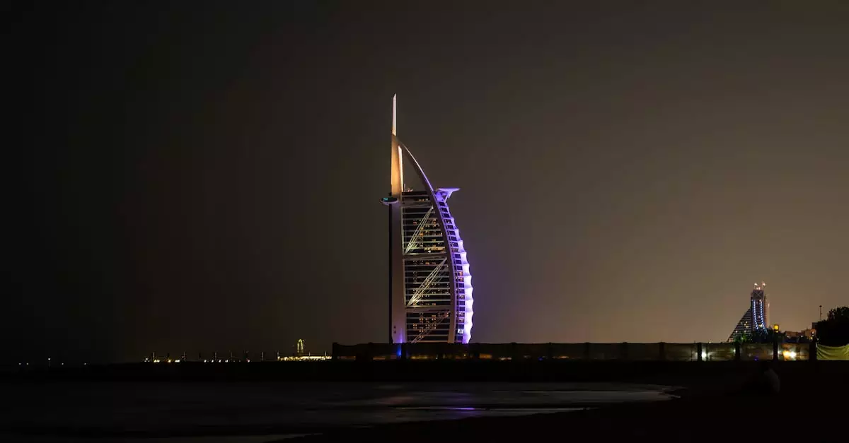 Modern sail shaped building with neon lights located on shore of calm sea against cloudless night sky in Dubai