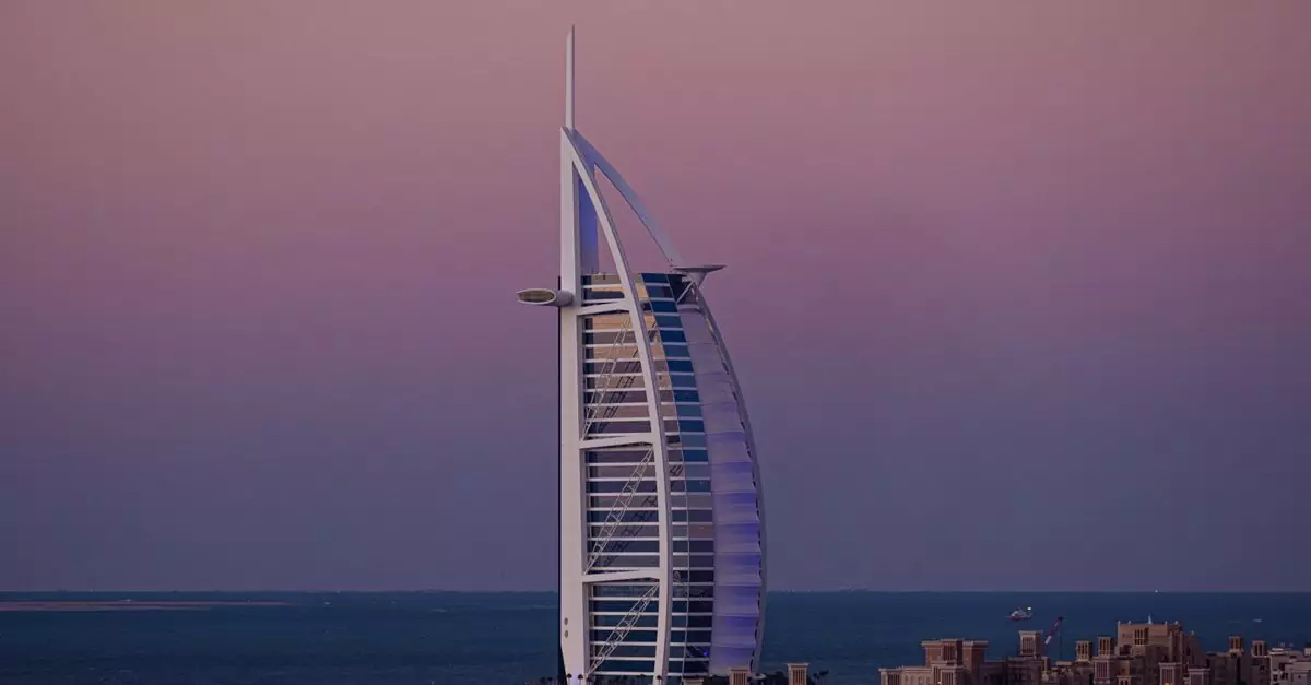 Scenery view of Burj Al Arab skyscraper hotel surrounded by small houses and blue endless ocean at sundown