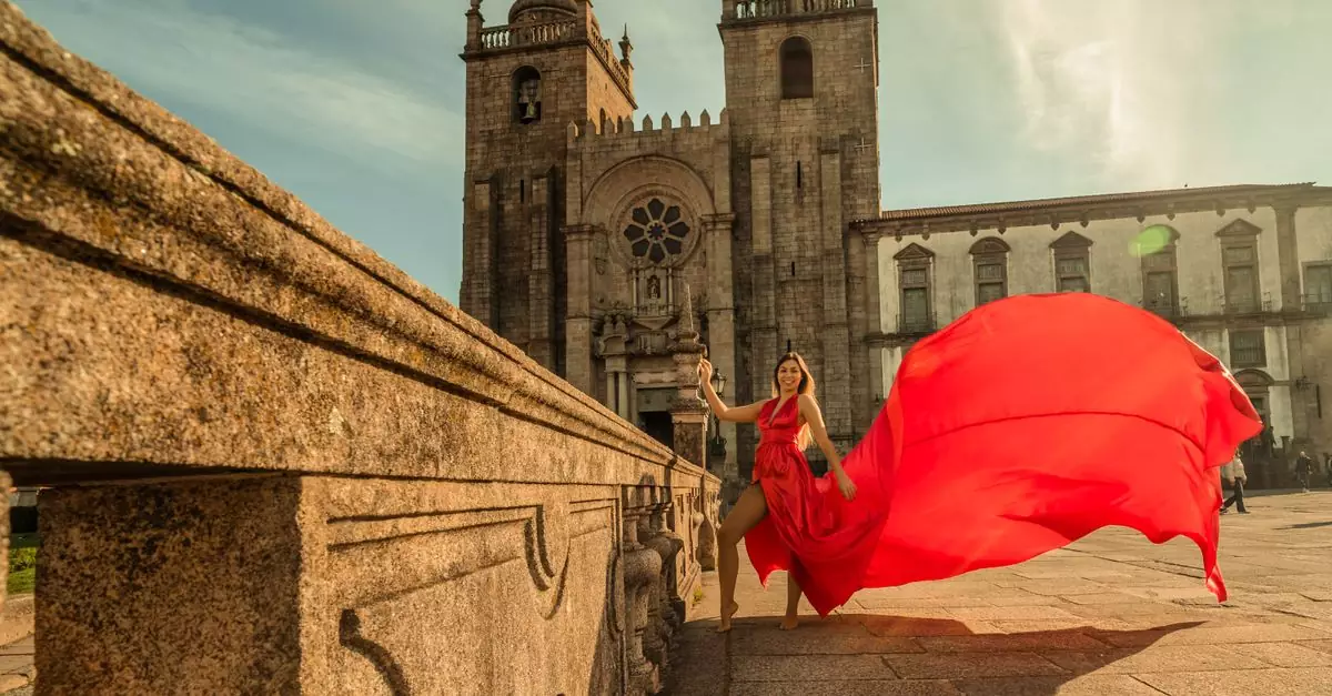 A woman in a red dress poses at Porto Cathedral in Portugal on a sunny day.