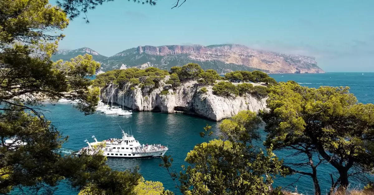 Breathtaking view of Cassis coast featuring a white yacht and lush greenery under a clear blue sky.