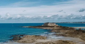 Breathtaking view of a historic fortress on the rocky coastline of Saint-Malo, France under a vibrant blue sky.