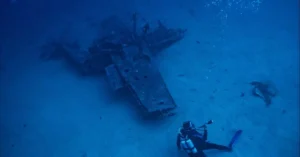 A scuba diver explores a submerged shipwreck deep underwater, capturing adventure and exploration.