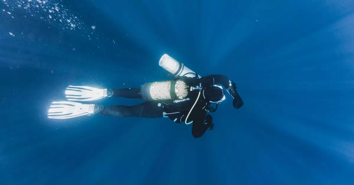 From above of fit anonymous diver in flippers with oxygen cylinder on back exploring blue ocean water with bubbles during vacation