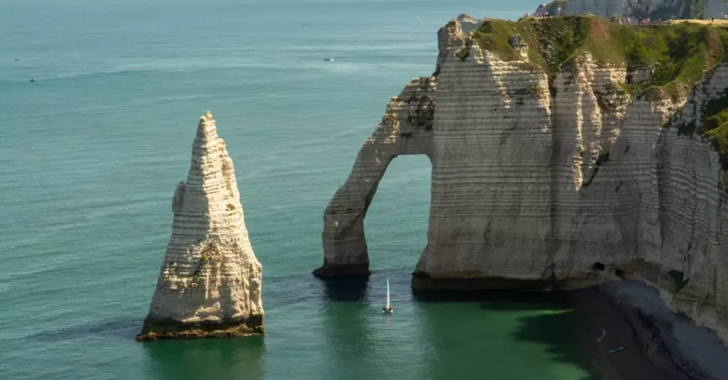 Étretat Cliffs France Guide: Normandy's Natural Wonders 10 Breathtaking view of chalk cliffs and sea arch at Étretat, Normandy, France with a distant sailboat.