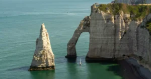 Breathtaking view of chalk cliffs and sea arch at Étretat, Normandy, France with a distant sailboat.