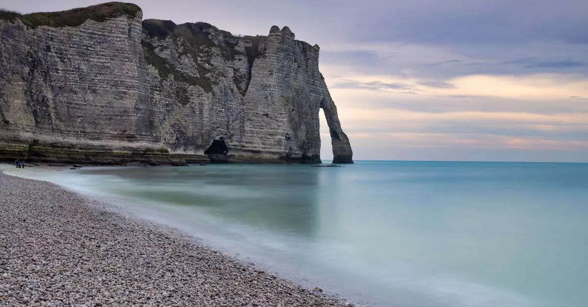 Beautiful view of Étretat cliffs, Normandy, France at dusk with calm sea and beach pebbles.