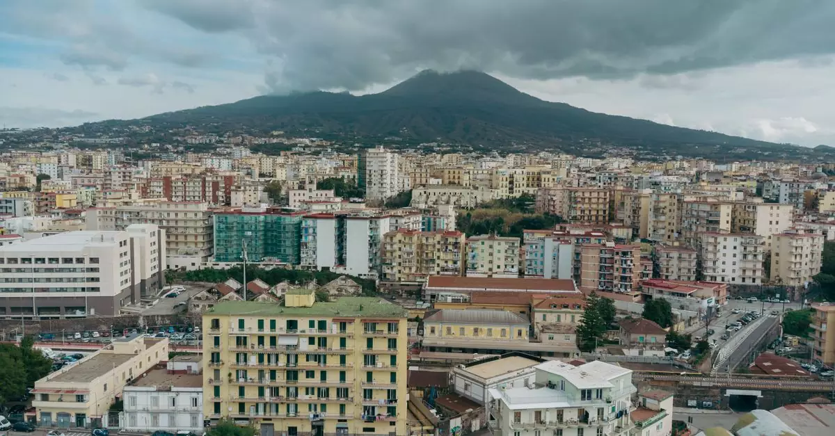 Aerial view of Naples cityscape with the towering Mount Vesuvius under a cloudy sky.