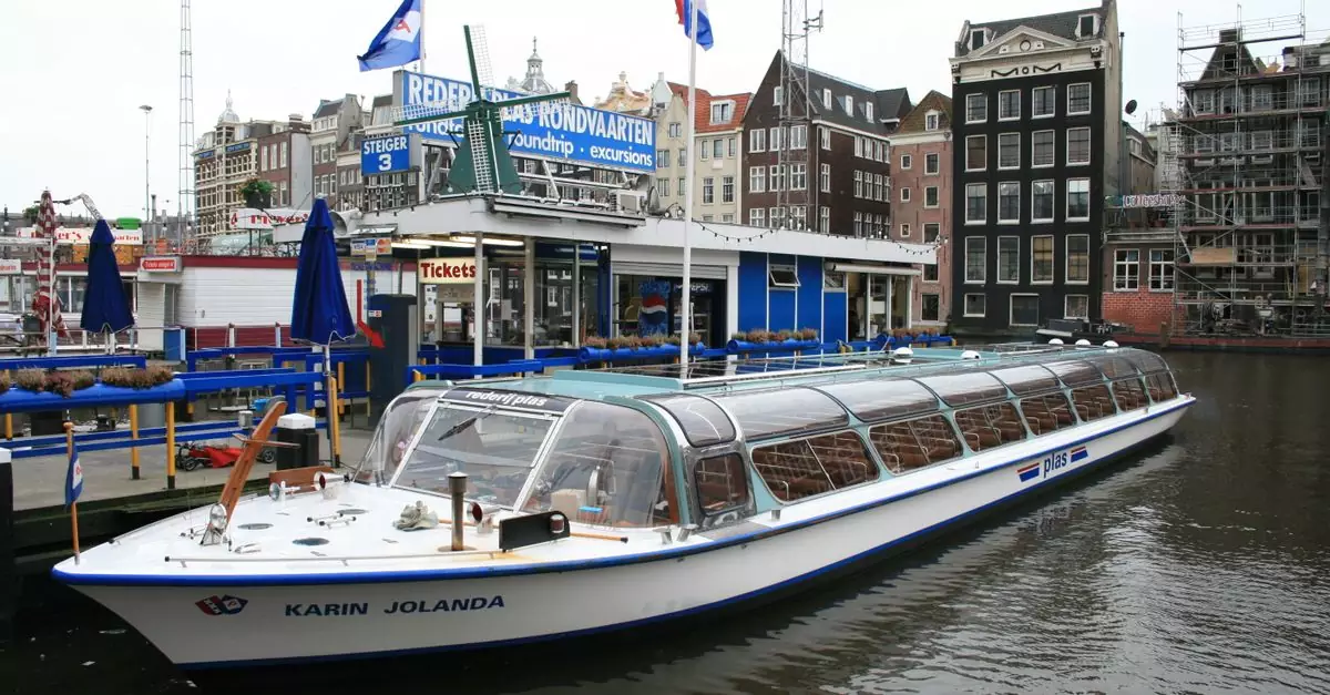 Amsterdam canal boat docked near historical buildings on a cloudy day.