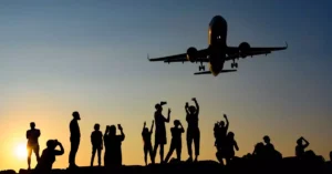 A dynamic silhouette of people photographing an airplane during a vibrant sunset.