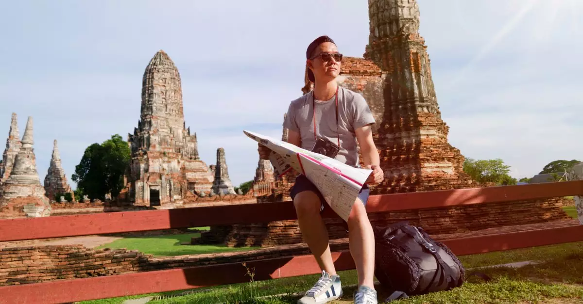 Man studying map amidst ancient temple ruins in Thailand, highlighting travel and exploration.