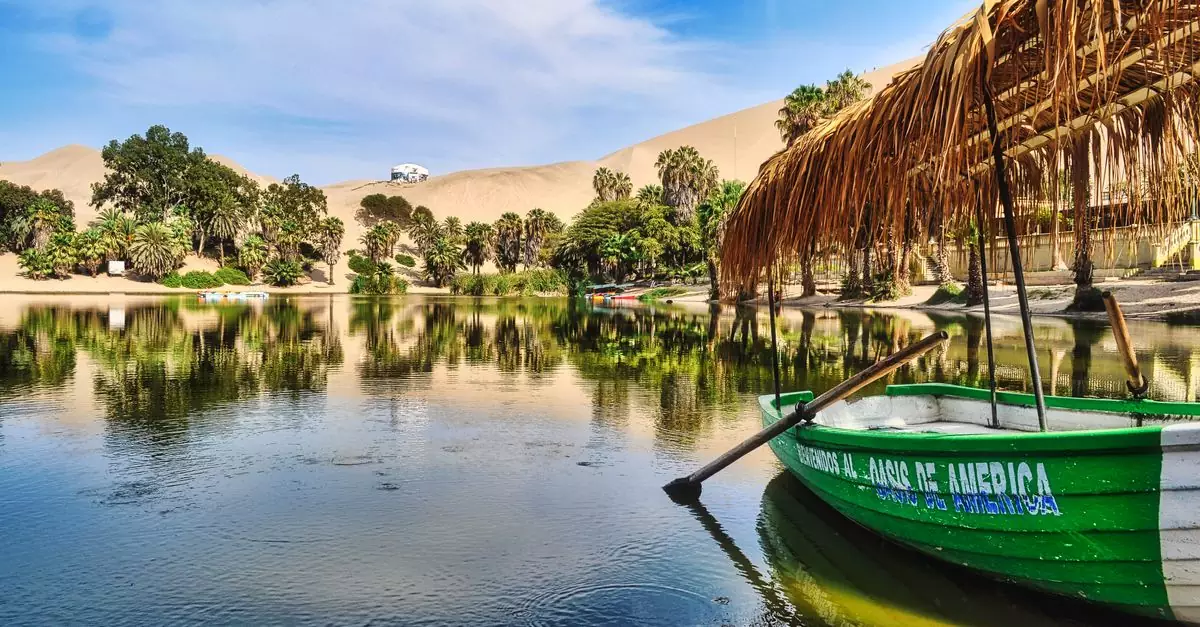 Tranquil view of the Huacachina oasis with reflections, palm trees, and sand dunes in Ica, Perú.
