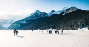 People enjoy ice skating on frozen Lake Louise in Banff National Park, surrounded by snow-covered mountains.
