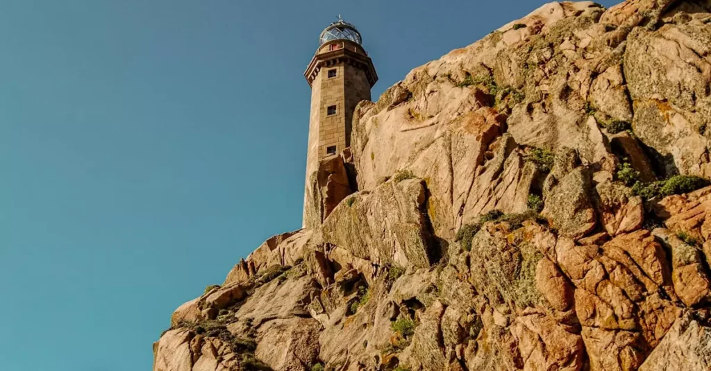Lighthouse perched on rugged cliffs with a clear blue sky, perfect for travel and adventure themes.