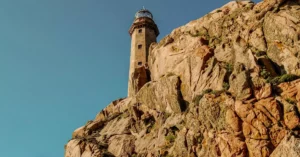 Lighthouse perched on rugged cliffs with a clear blue sky, perfect for travel and adventure themes.