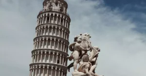 View of the Leaning Tower of Pisa with a nearby classical statue under a clear sky.