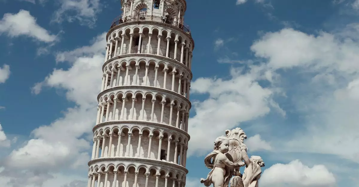 Capture of the iconic Leaning Tower of Pisa alongside classical statues under a blue sky with clouds.