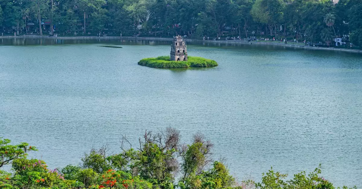 A scenic view of Turtle Tower on Hoan Kiem Lake surrounded by lush greenery in Hanoi, Vietnam.
