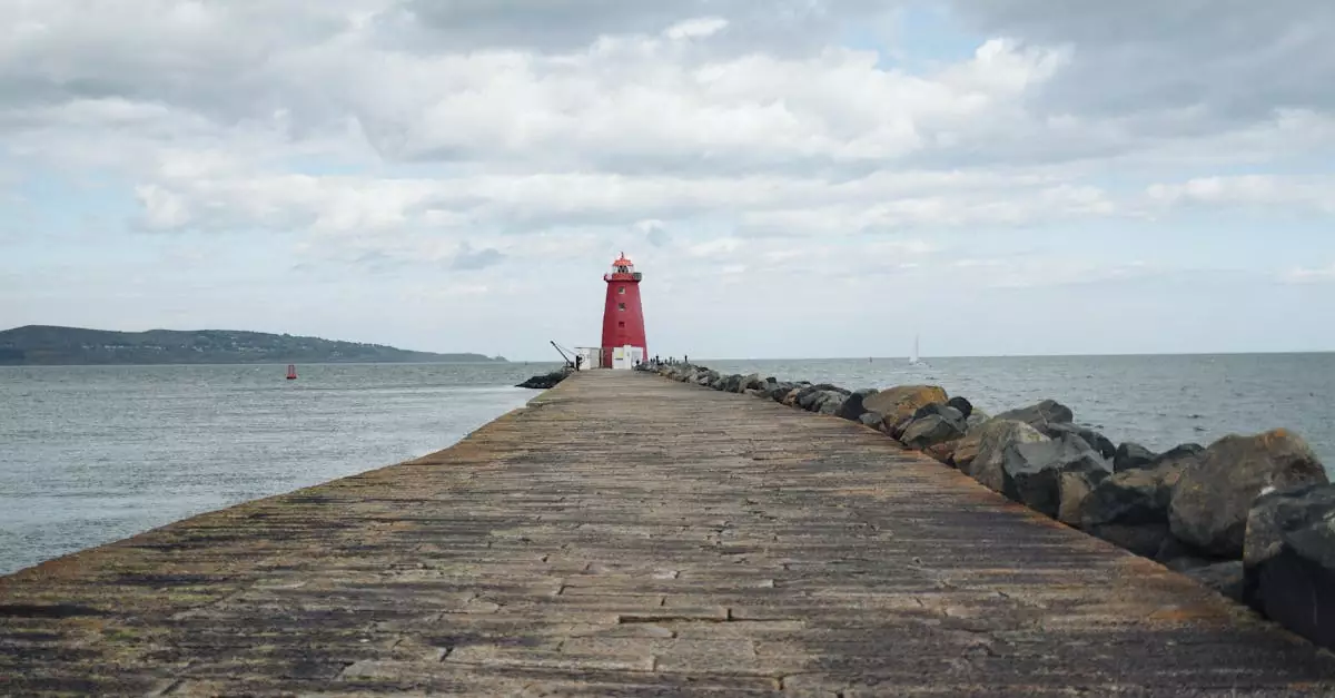 A red lighthouse stands at the end of a rocky pier under a cloudy sky by the sea.