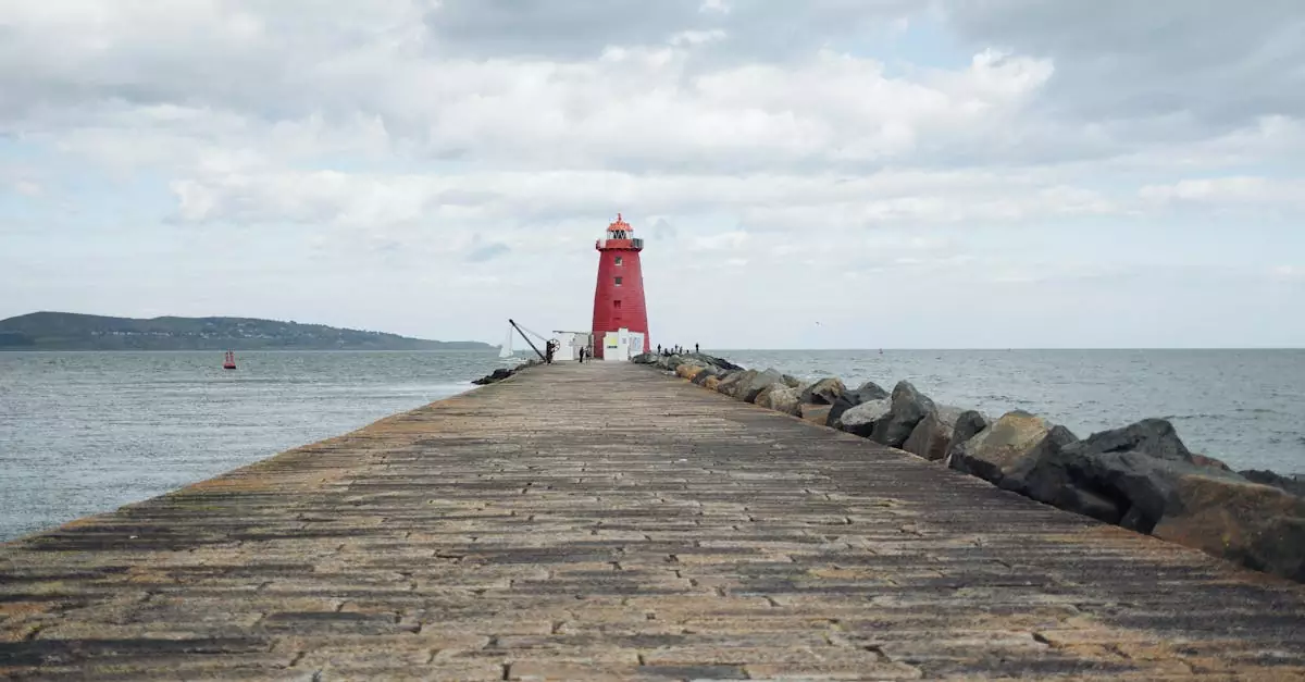 Scenic view of a red lighthouse on a long pier extending into the ocean under cloudy skies.