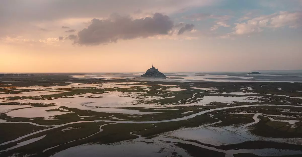 Stunning aerial view of Le Mont-Saint-Michel during low tide at sunset with reflective marshlands.