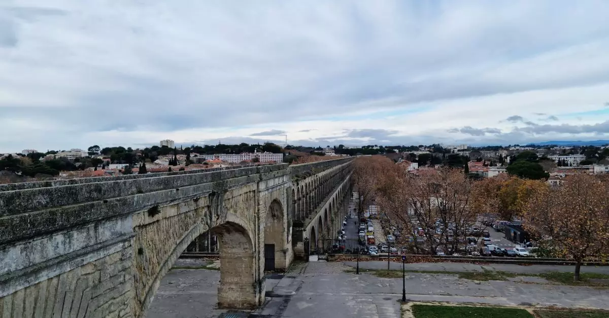 A scenic view of the historic Aqueduc Saint-Cl&eacute;ment in Montpellier, showcasing its arches under a cloudy sky.
