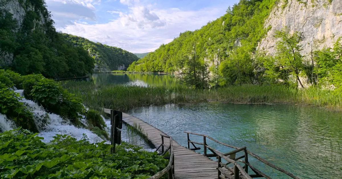 Explore the scenic beauty of Plitvice Lakes National Park with a wooden pathway, waterfalls, and lush greenery.