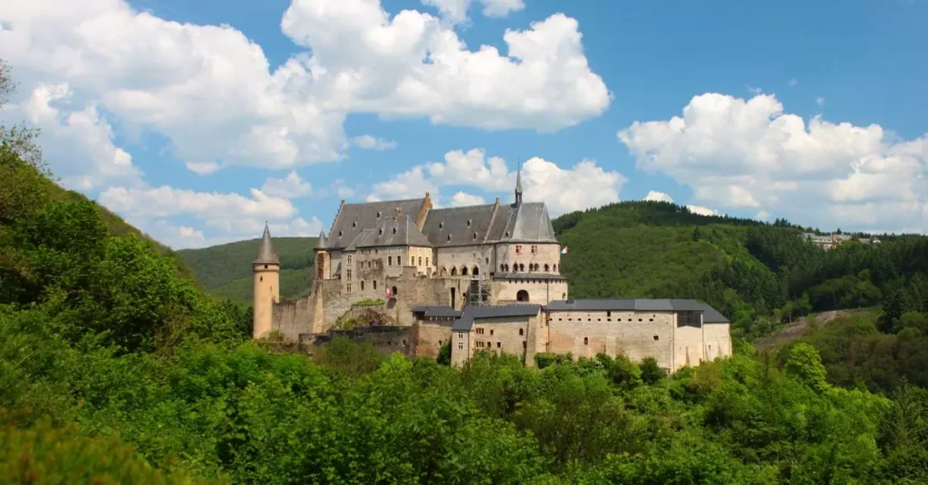 Explore the historical Vianden Castle amidst Luxembourg's lush greenery under a bright sky.