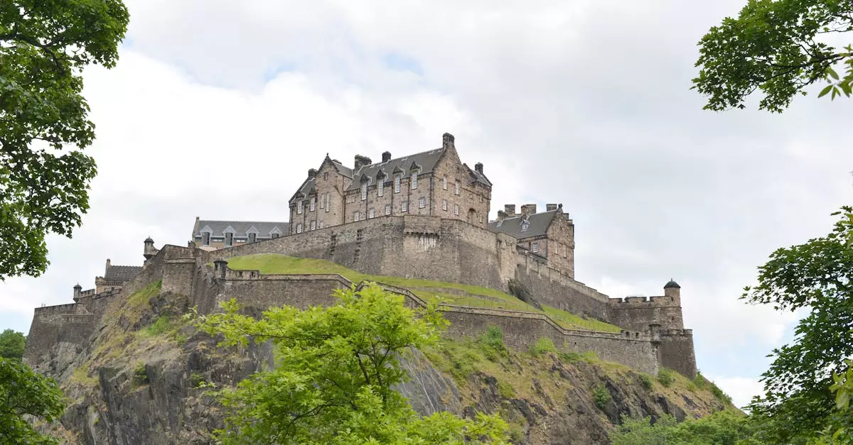 View of the iconic Edinburgh Castle perched on Castle Rock, framed by trees under a cloudy sky.