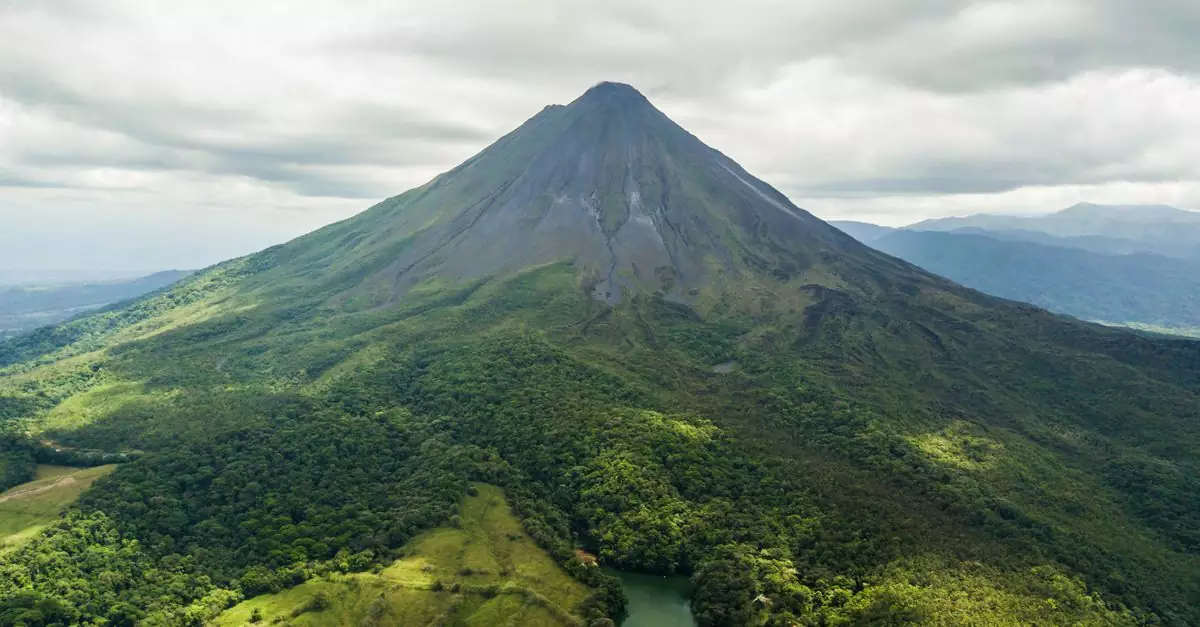 Dramatic aerial view of the lush green Arenal Volcano in Costa Rica against a cloudy sky.