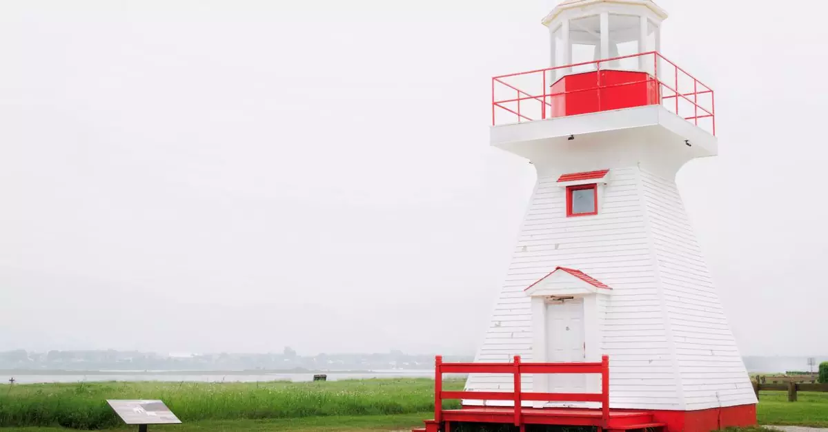 A charming red and white lighthouse stands on a tranquil seaside landscape.