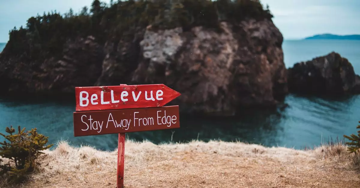 Bright warning sign urging stay away from edge located on precipice with cliff covered with trees on background