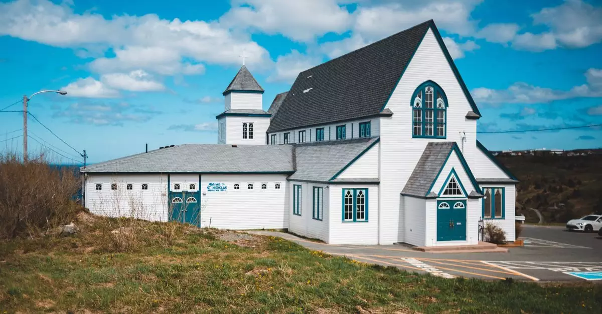 Exterior of aged traditional Saint Nicholas Anglican Church located in grassy valley in Torbay town against cloudy blue sky