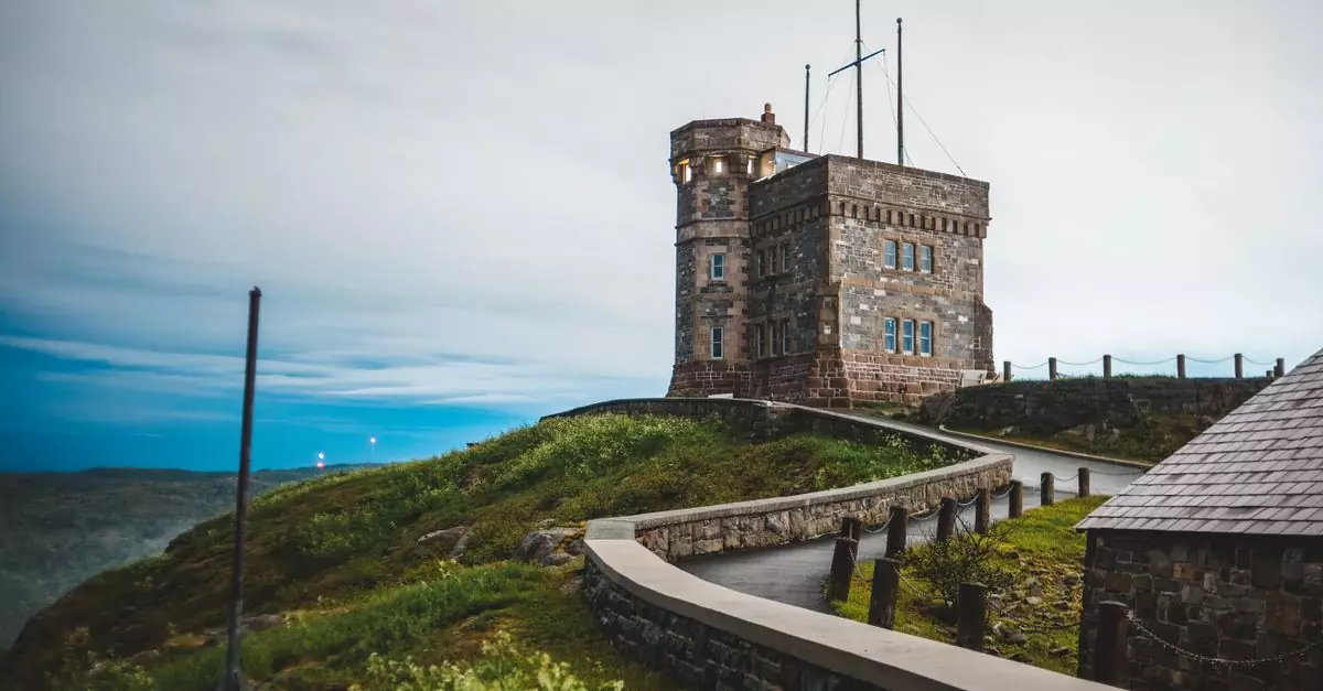 Overcast sky over small dark brown Cabot Tower surrounded by slopes covered with colorful green grass in St Johns in Newfoundland and Labrador in Canada