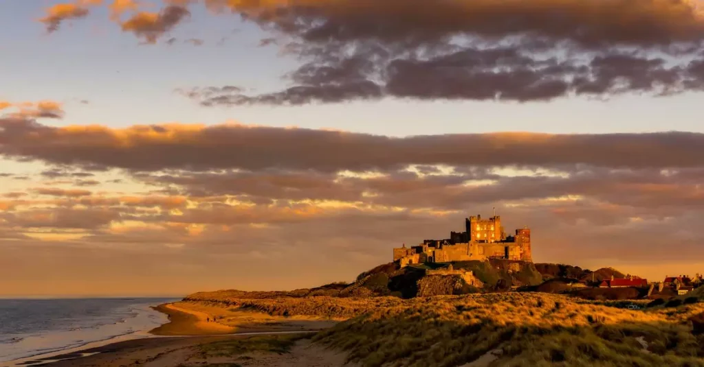 Stunning sunset over Bamburgh Castle with a sandy beach and dramatic clouds in England.